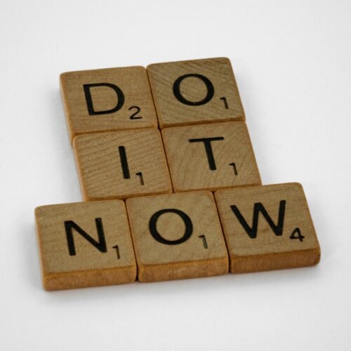 Wooden scrabble tiles forming 'DO IT NOW' on a minimal white backdrop. Inspiring concept.